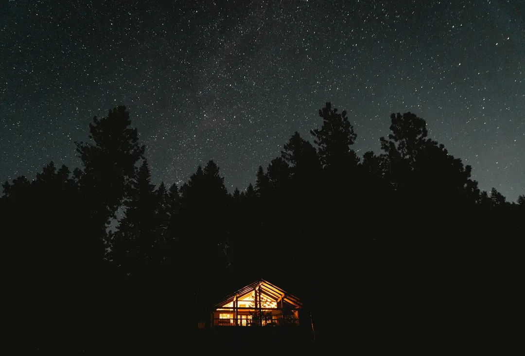 Beleuchtetes Gästehaus vor dunklem Tannenwald unter sternklarem Himmel