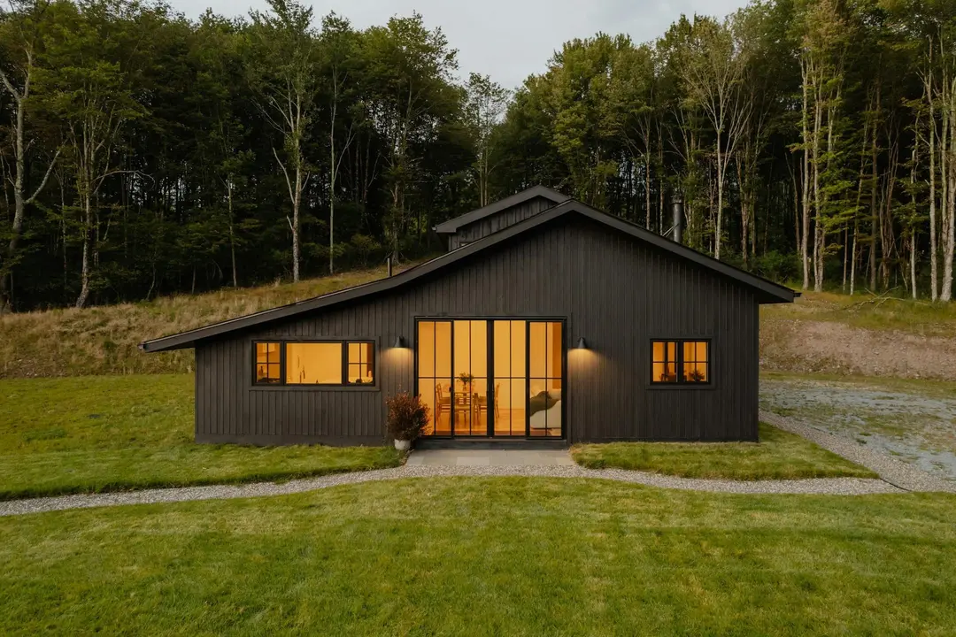 Haus Sternwald von der Wiese aus: schwarz verschaltes Holzhaus mit leuchtenden Glastüren am Waldrand