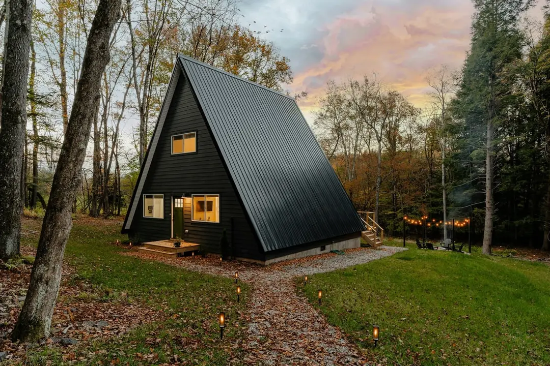 Schwarzes Giebelhaus mit warmen Fenstern und Laternenweg im Herbstwald